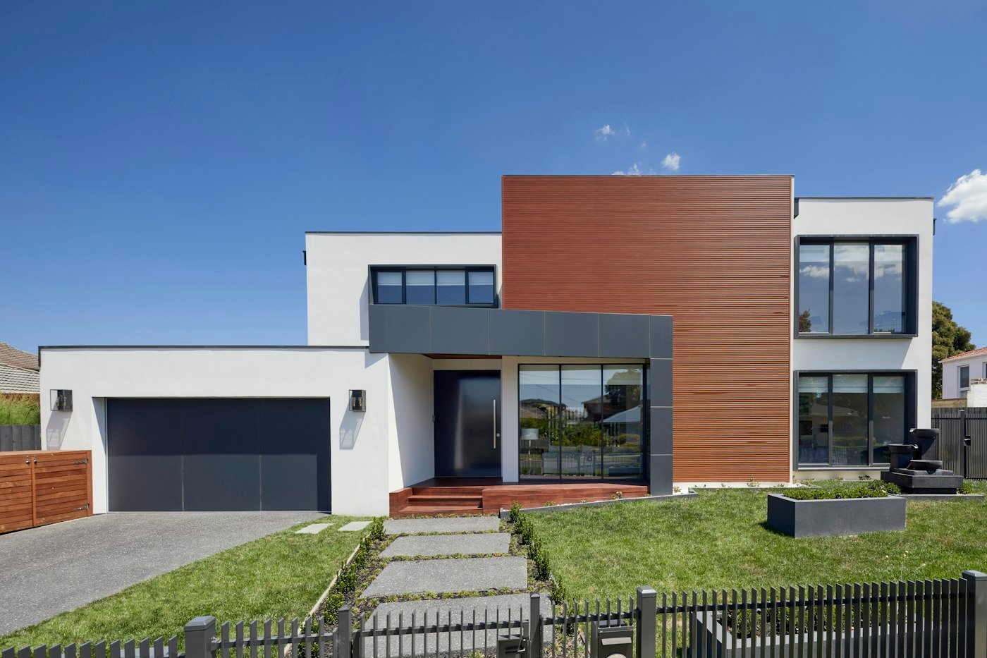 A white modern house with a timber panel, a dark front door, and a path across the lawn
