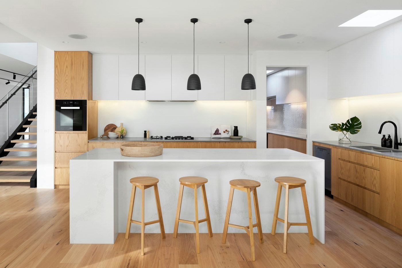 A white kitchen island with four wooden stools, wood cupboards, and black pendant lights