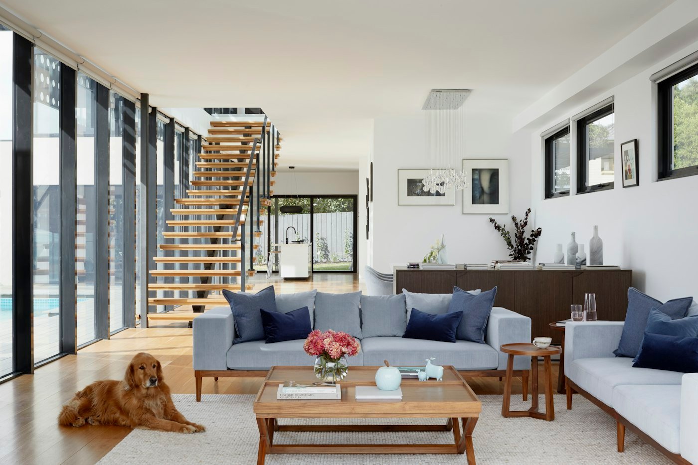 A bright living room with a pale blue sofa, a wooden staircase, and a dog lying on the floor